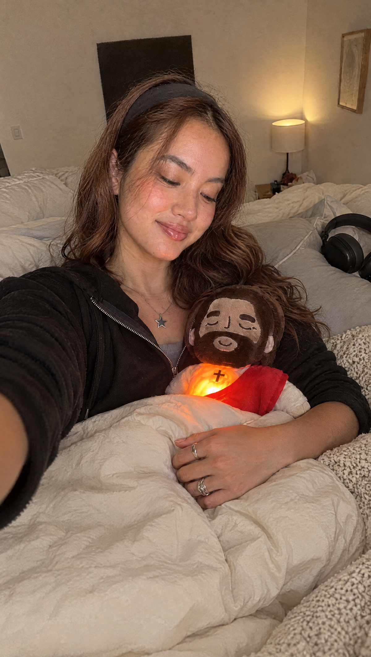 Woman cuddling the glowing Jesus plush in bed